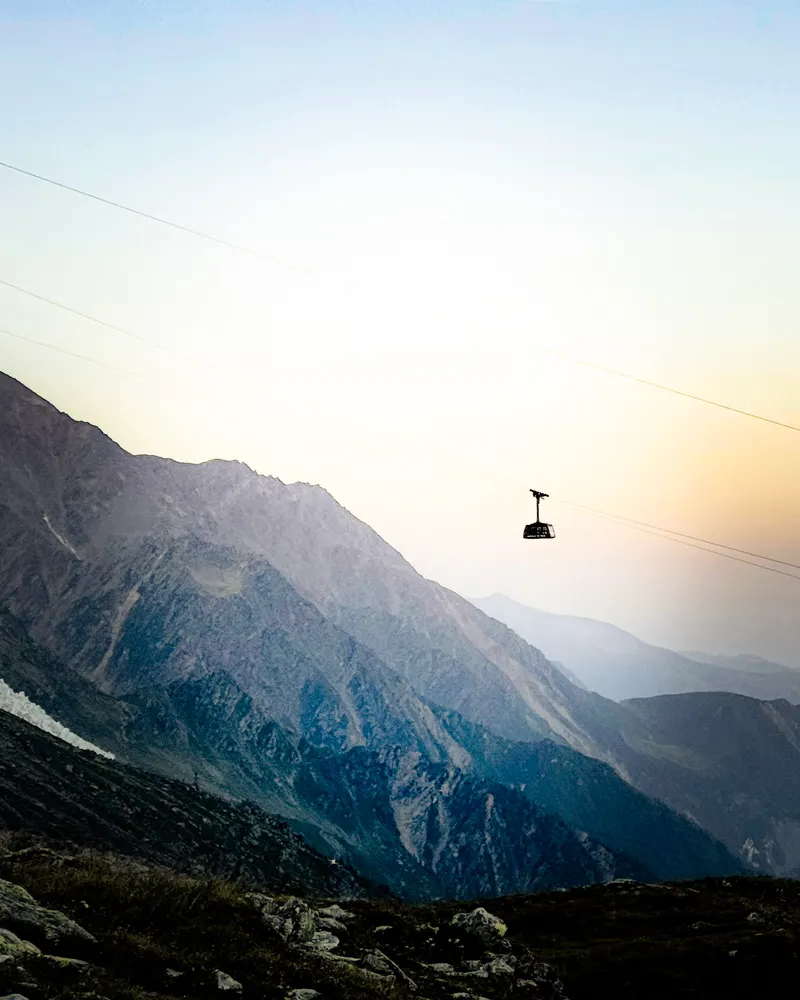 A cable car hanging over a mountain valley in hazy evening light.