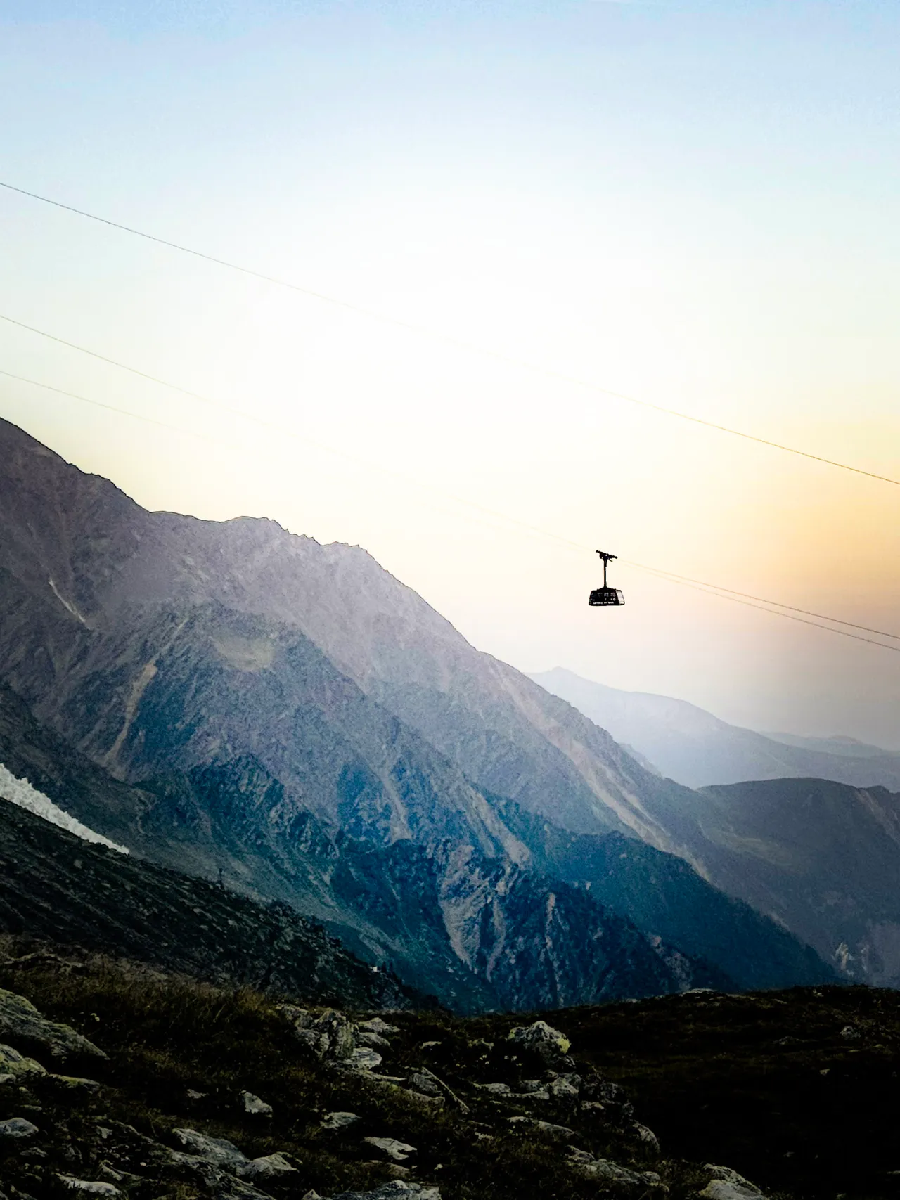 A cable car hanging over a mountain valley in hazy evening light.