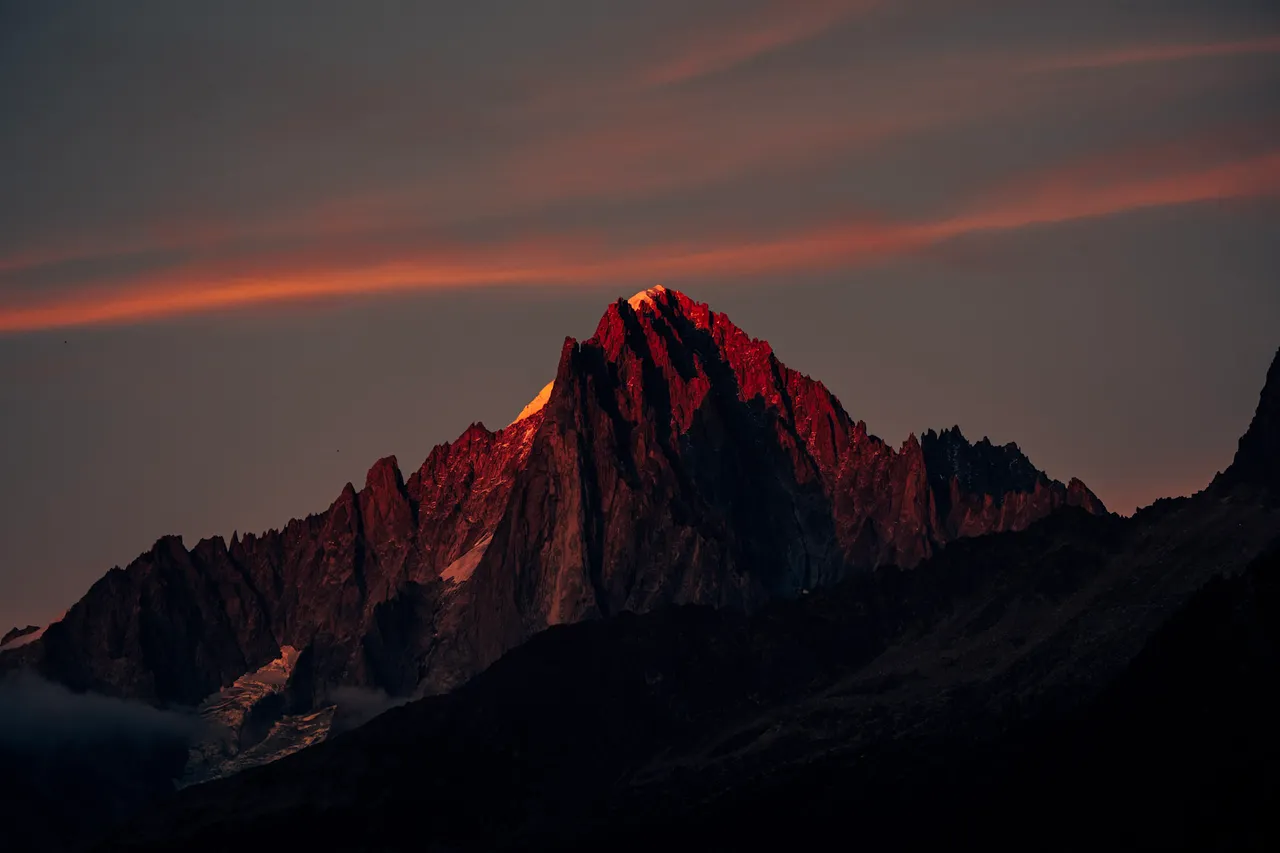 A rocky alpine summit lit red by the last of the evening light, with streaks of orange cloud in the sky above.