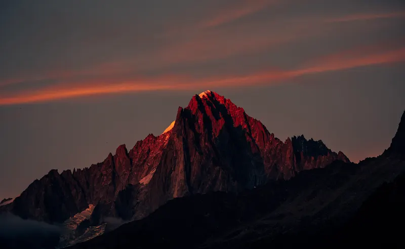 A rocky alpine summit lit red by the last of the evening light, with streaks of orange cloud in the sky above.