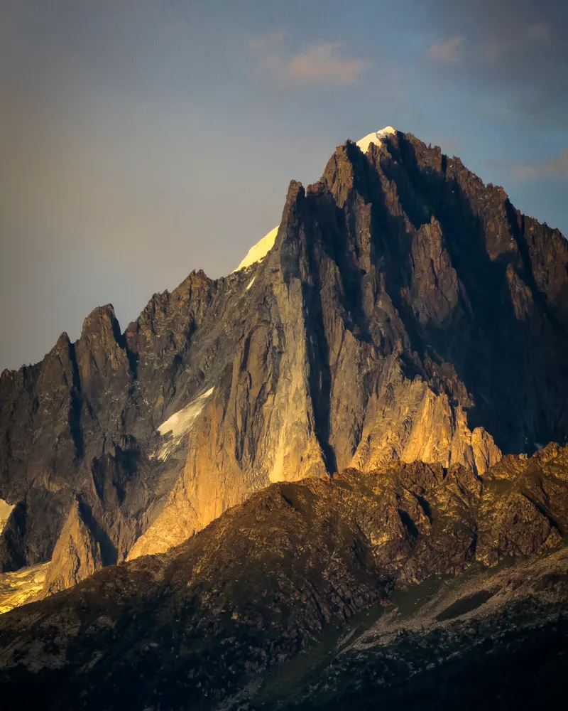 A steep rock peak lit gold by the last of the sun, above a darkening valley.