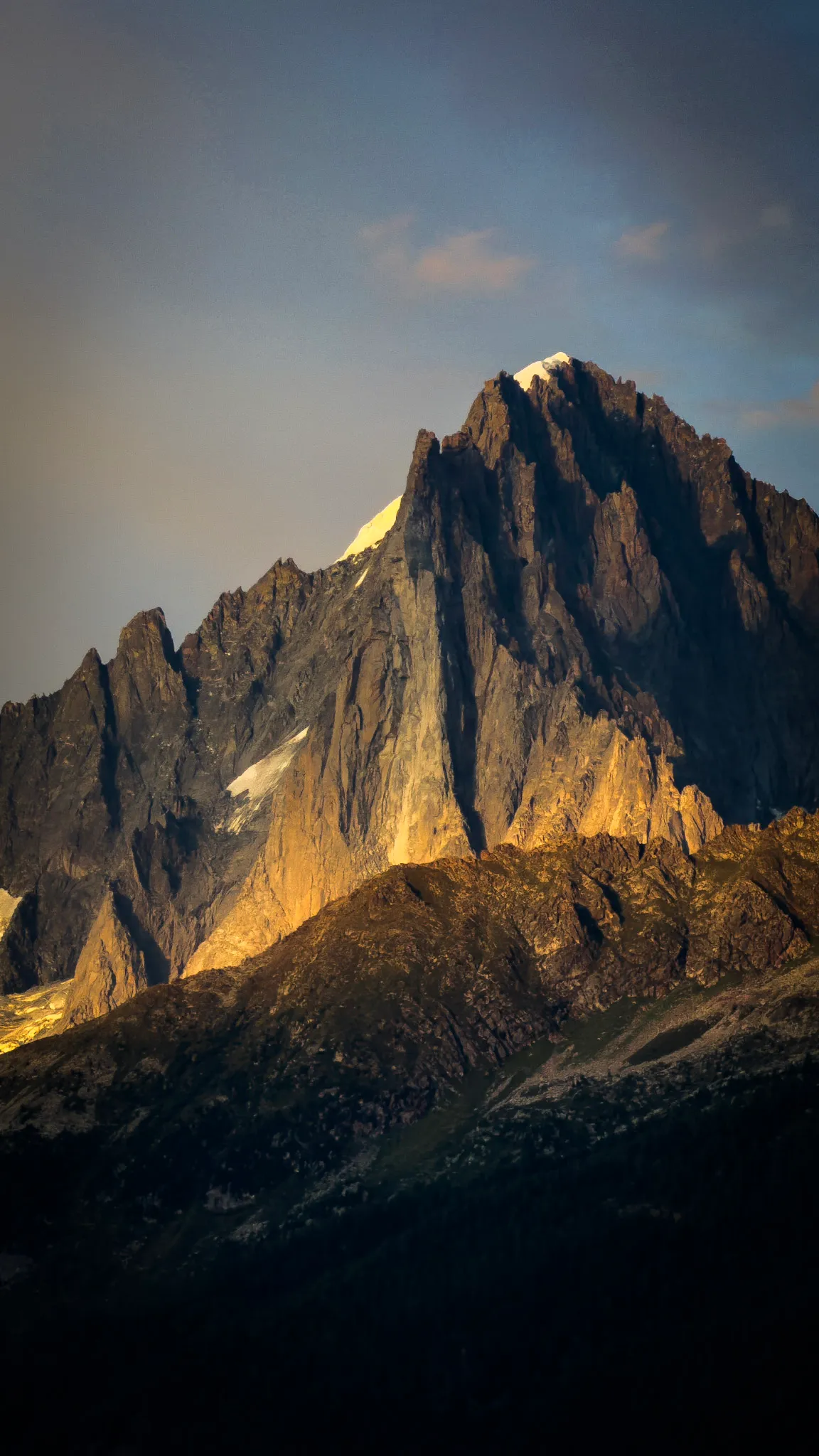 A steep rock peak lit gold by the last of the sun, above a darkening valley.