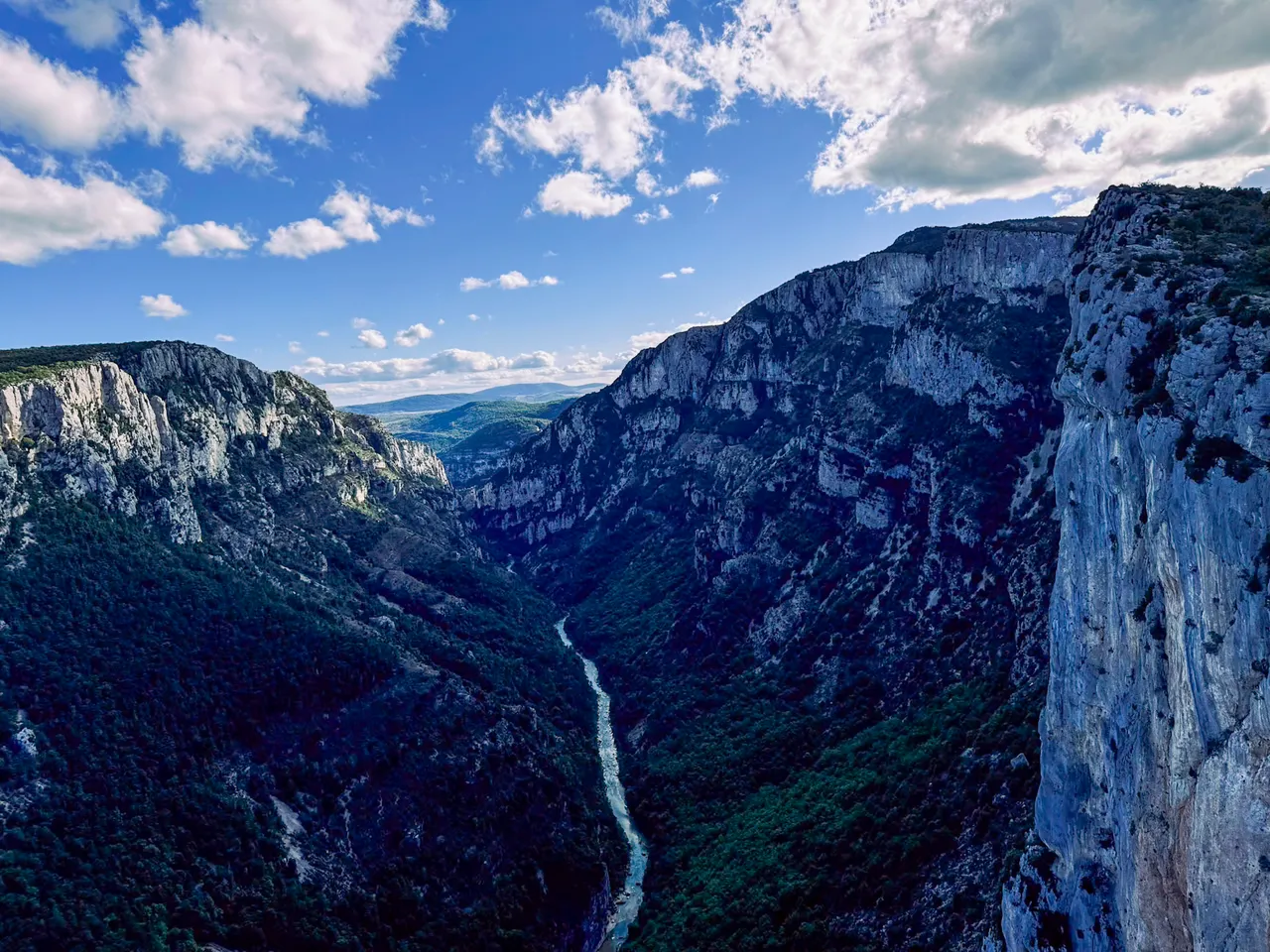 A deep river gorge between tall limestone cliffs, under a blue sky with big clouds.