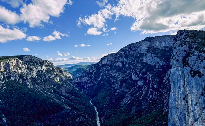 A deep river gorge between tall limestone cliffs, under a blue sky with big clouds.