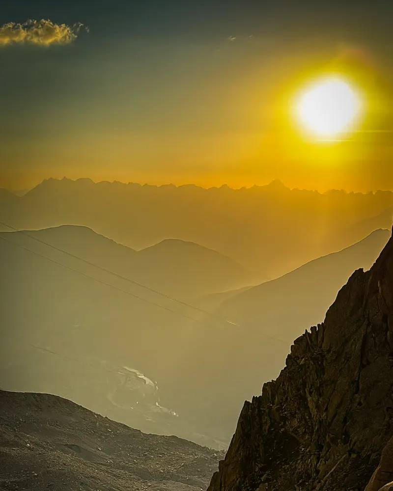 The sun low over hazy layers of mountain ridges, with dark rock in the foreground.