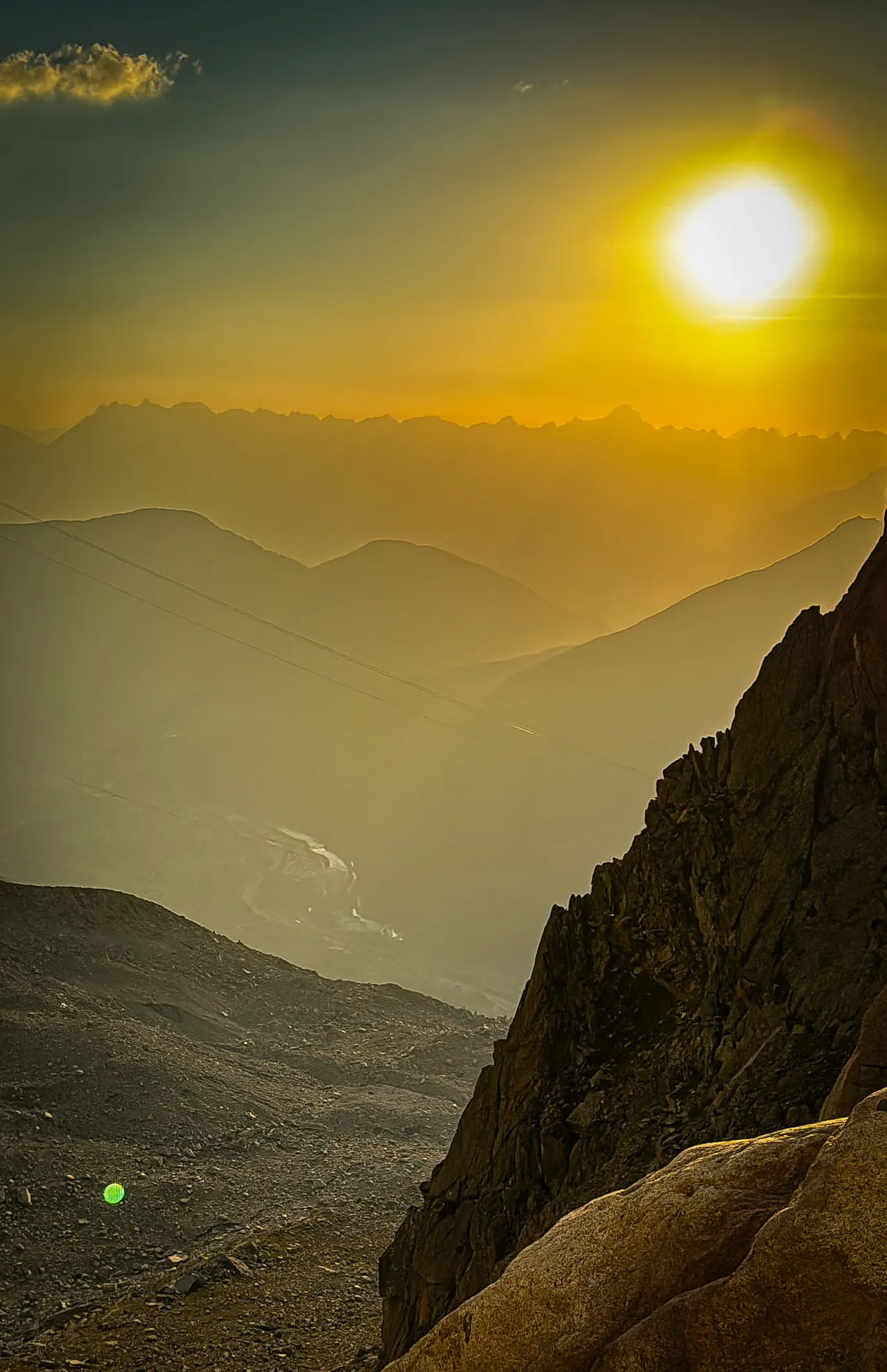 The sun low over hazy layers of mountain ridges, with dark rock in the foreground.