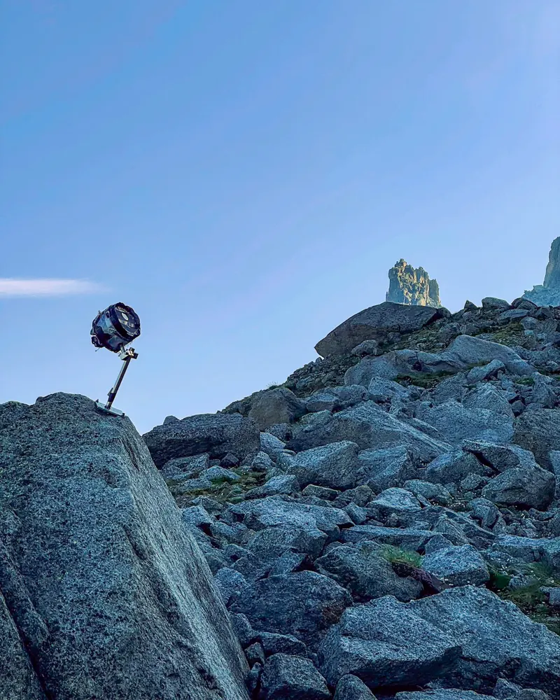 A small instrument on a pole, perched on a granite boulder, with a rock spire on the skyline behind.