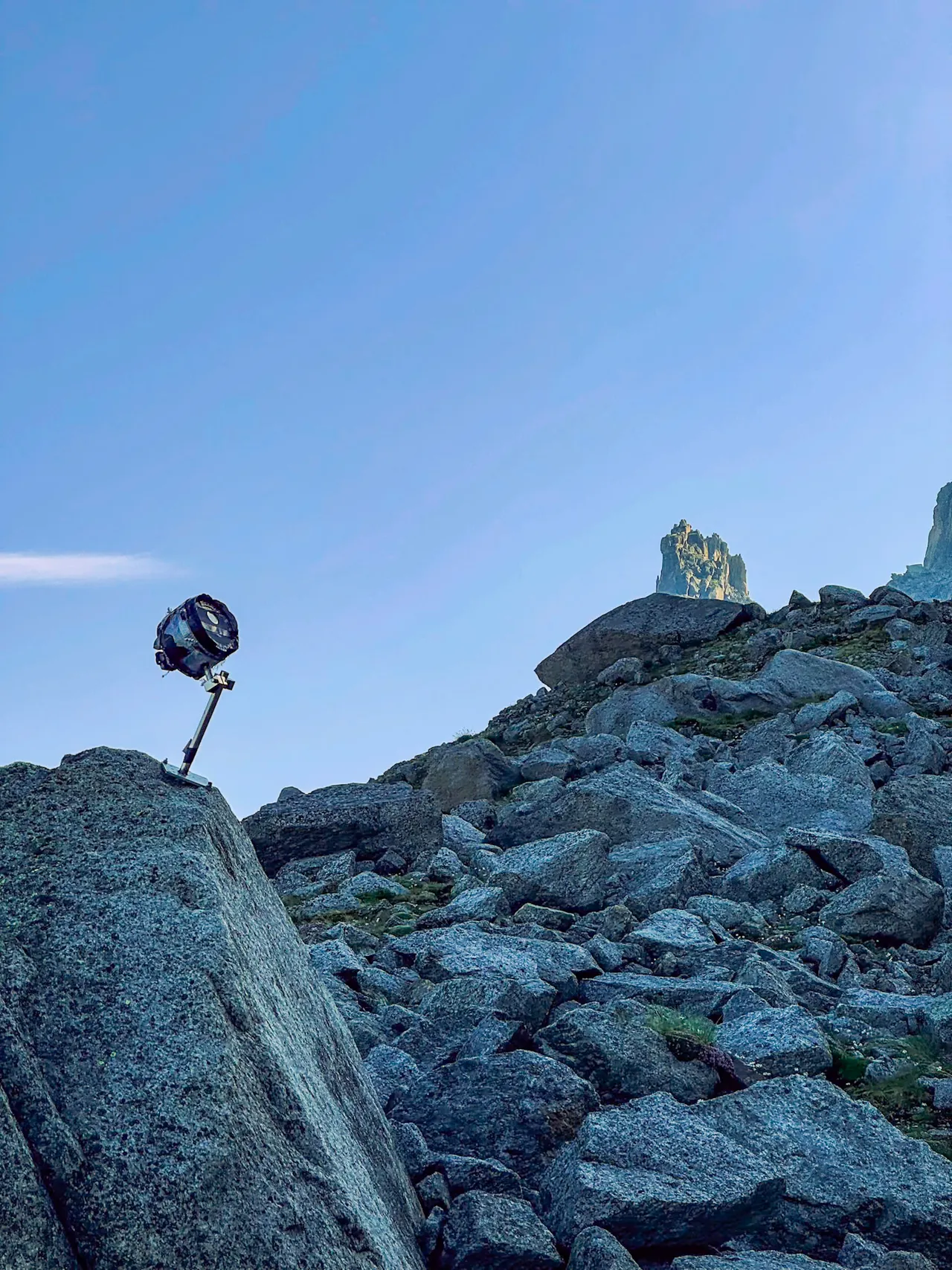 A small instrument on a pole, perched on a granite boulder, with a rock spire on the skyline behind.