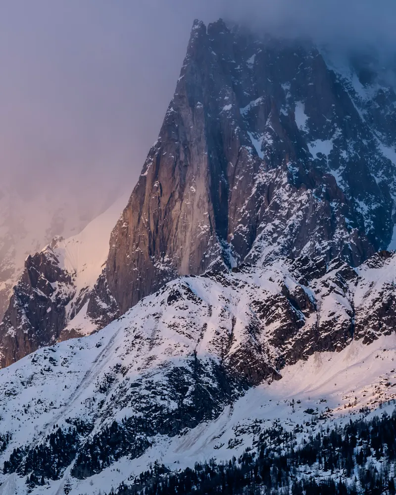 A rocky peak half hidden in cloud, with snow on the slopes below in soft evening colour.
