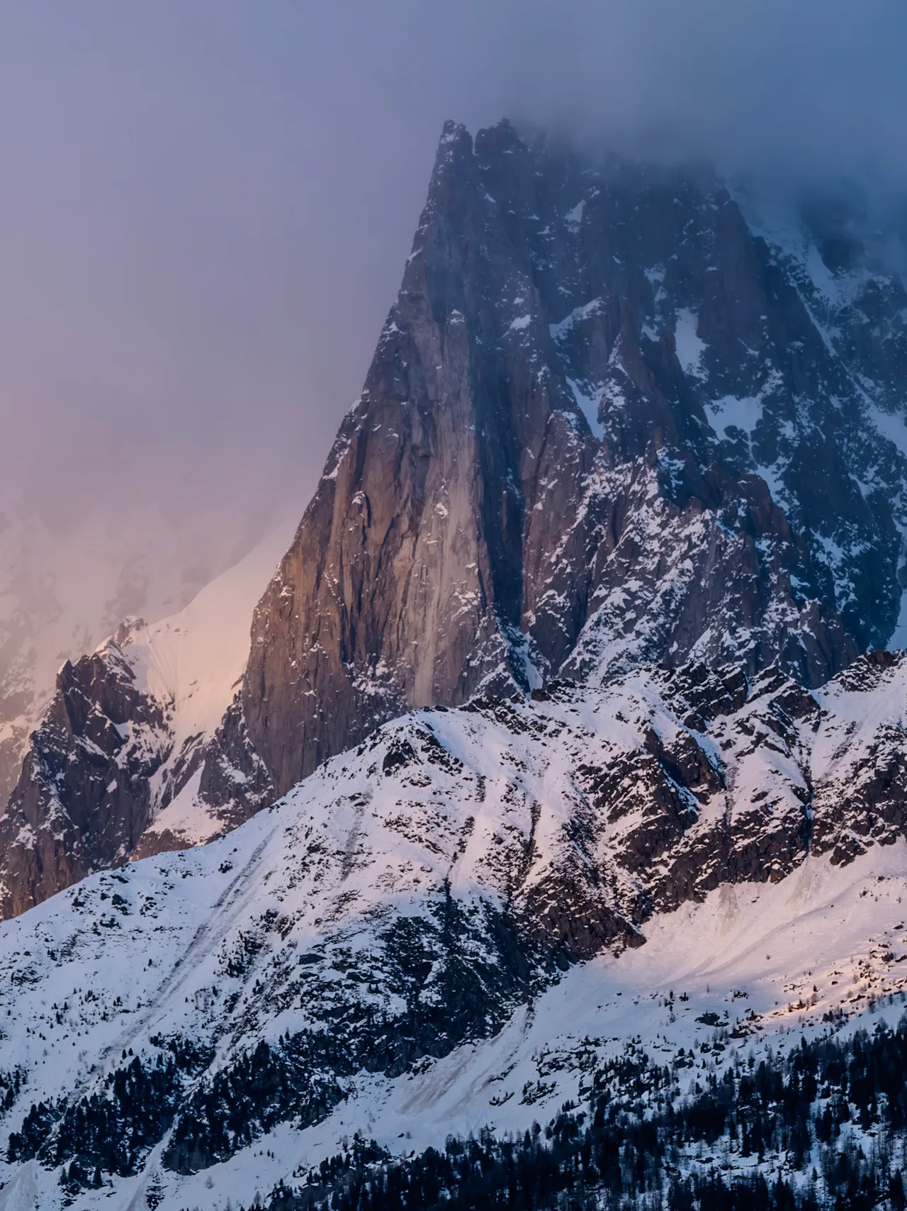 A rocky peak half hidden in cloud, with snow on the slopes below in soft evening colour.