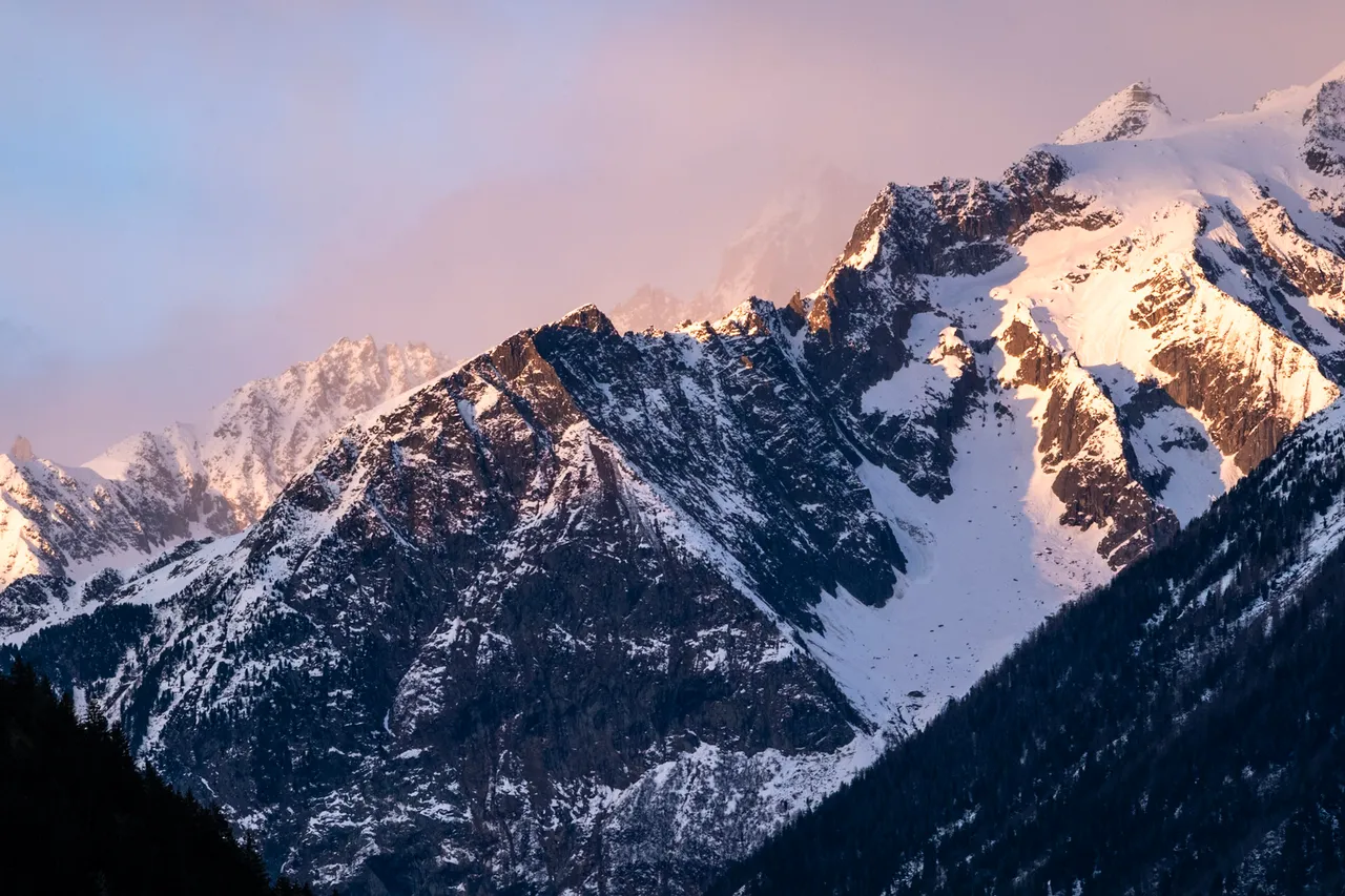 Snowy peaks glowing pink in the last light, with a layer of cloud behind.