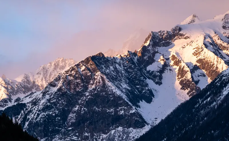 Snowy peaks glowing pink in the last light, with a layer of cloud behind.