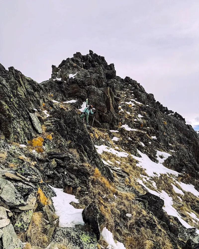 A dark, broken rock ridge dusted with snow under a pale cloudy sky.