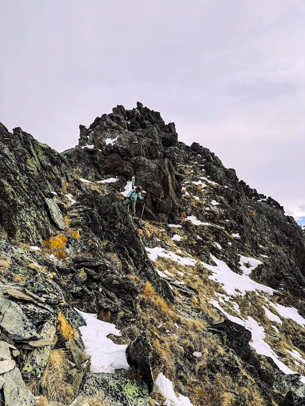 A dark, broken rock ridge dusted with snow under a pale cloudy sky.