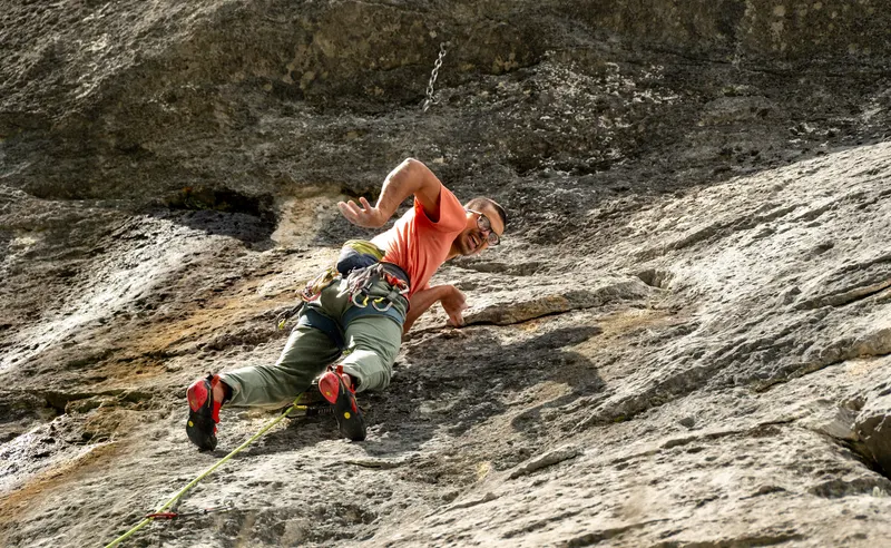 A climber in an orange shirt stretched out on a pale sloping rock slab.