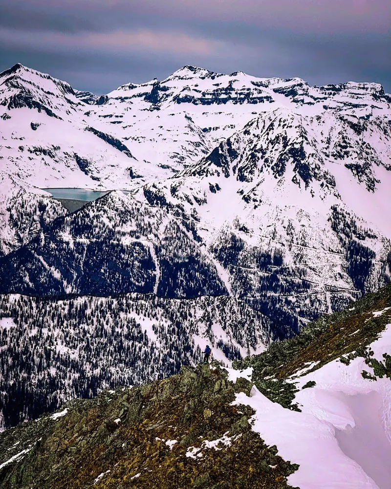 A snow-covered mountain range seen from a rocky ridge in winter.