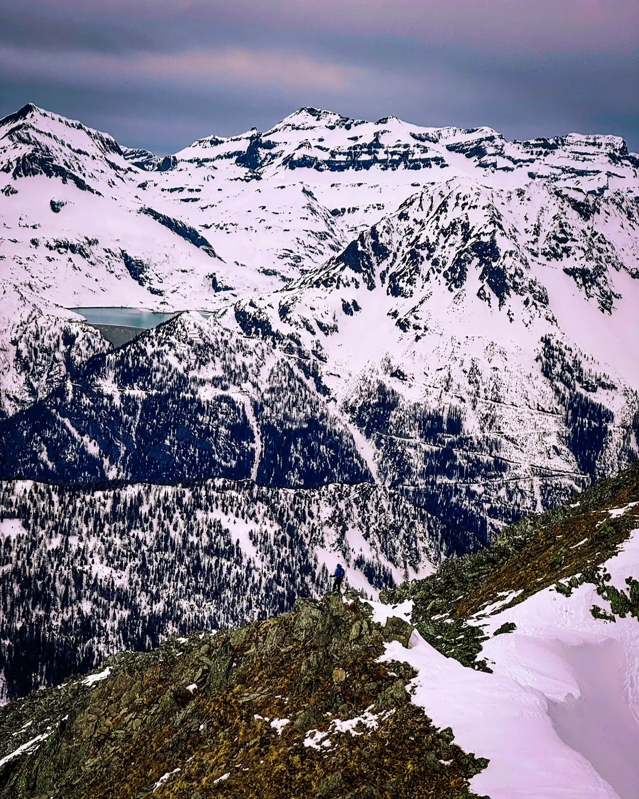 A snow-covered mountain range seen from a rocky ridge in winter.