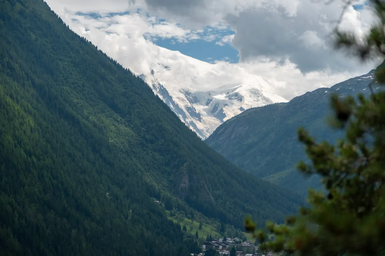 A steep forested valley with a glacier-topped peak showing between clouds.