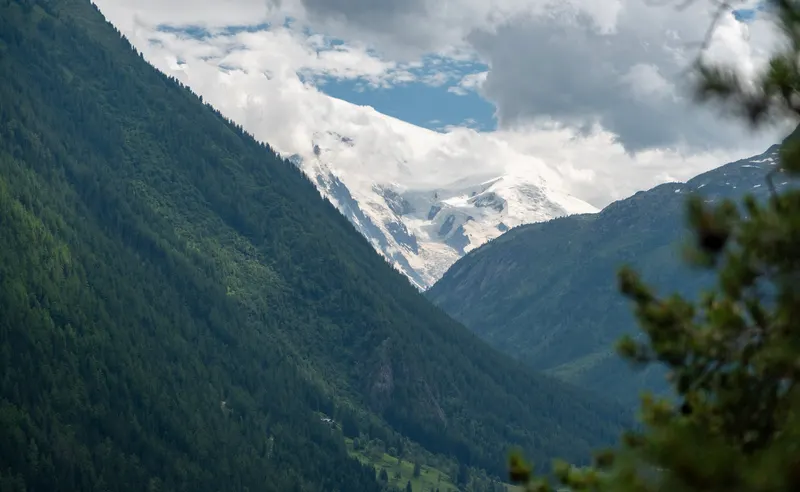 A steep forested valley with a glacier-topped peak showing between clouds.